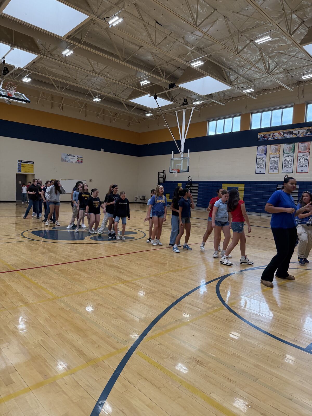 A group of students and an adult stand in a line on a polished wooden gymnasium floor.