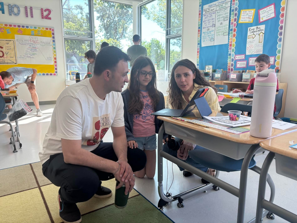A student and her two parents or guardians sit at a desk during a Math-in.
