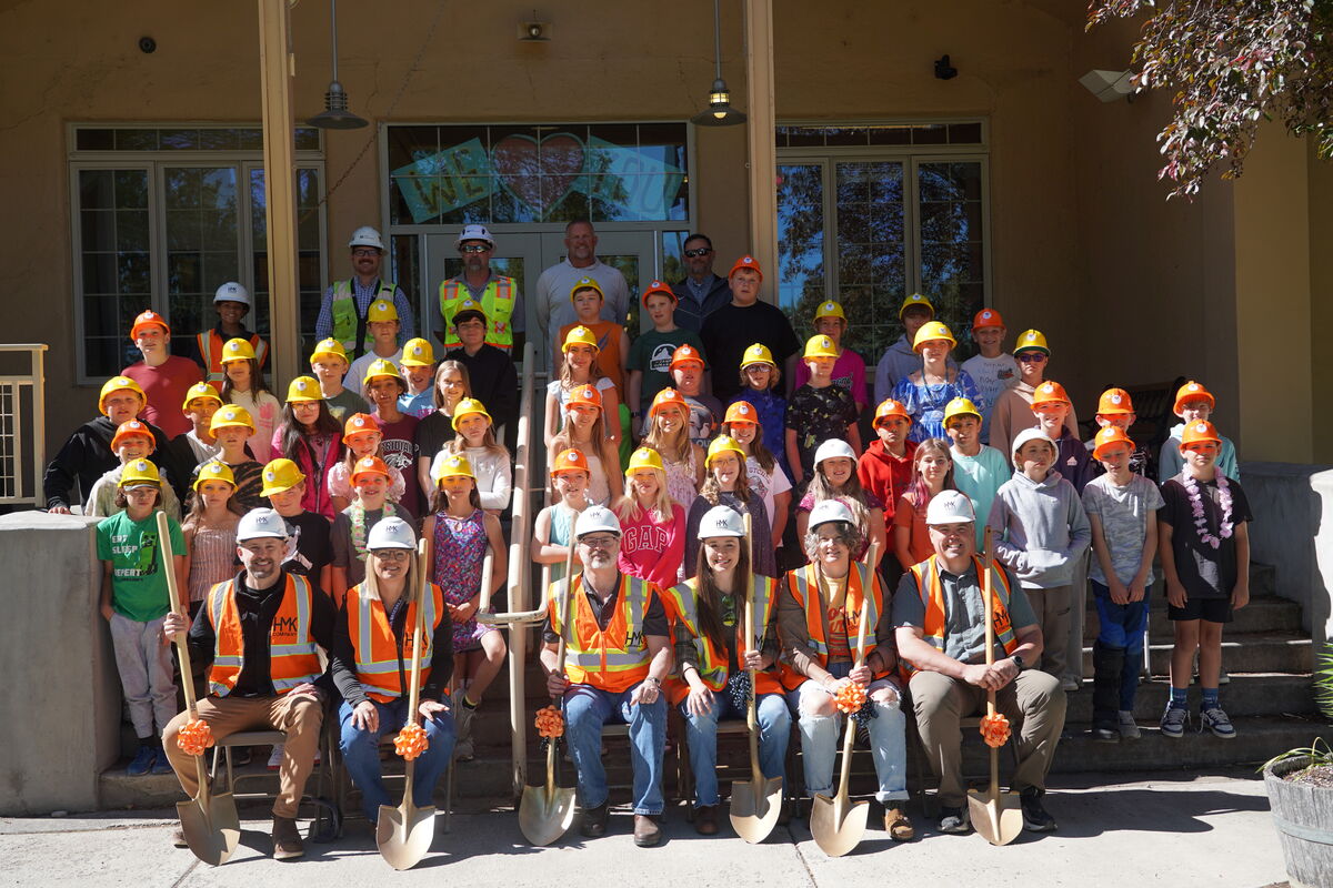 A large group of children and adults, many wearing hard hats and safety vests, pose for a photo outdoors.