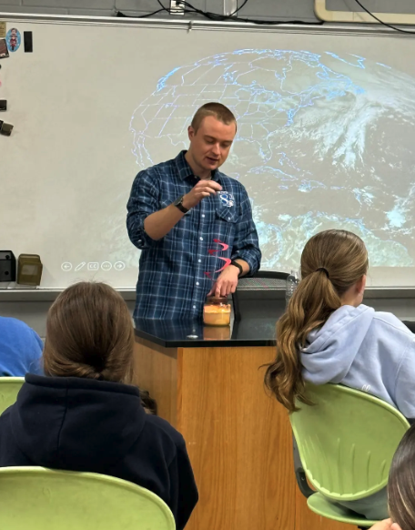 A teacher demonstrates a science experiment with a candle to students in a classroom.