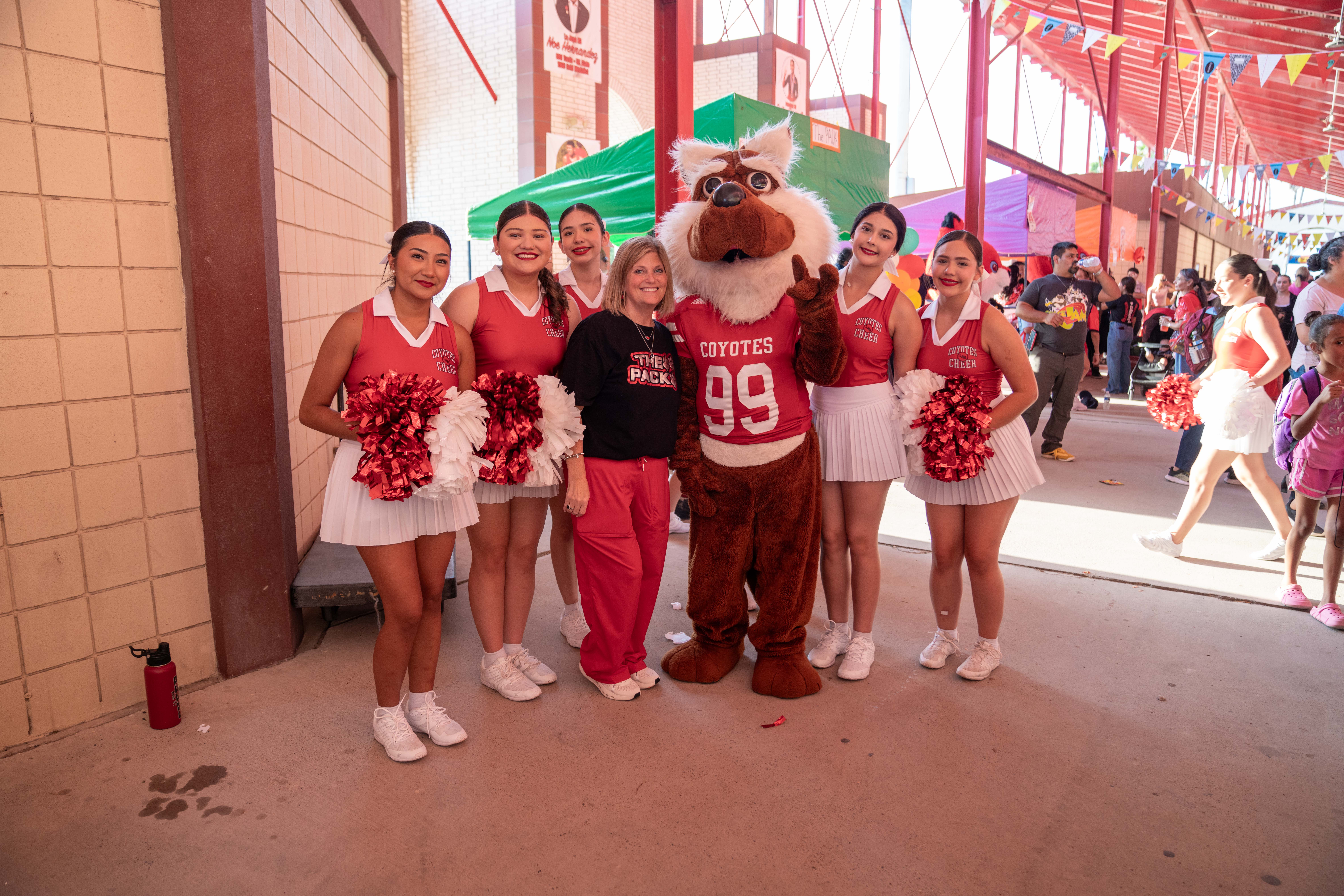 A group of cheerleaders in red and white uniforms pose with a mascot and a coach.