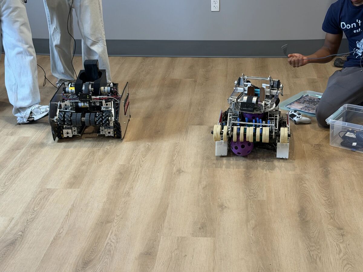 Two custom-built robots with intricate mechanisms sit on a wooden floor.
