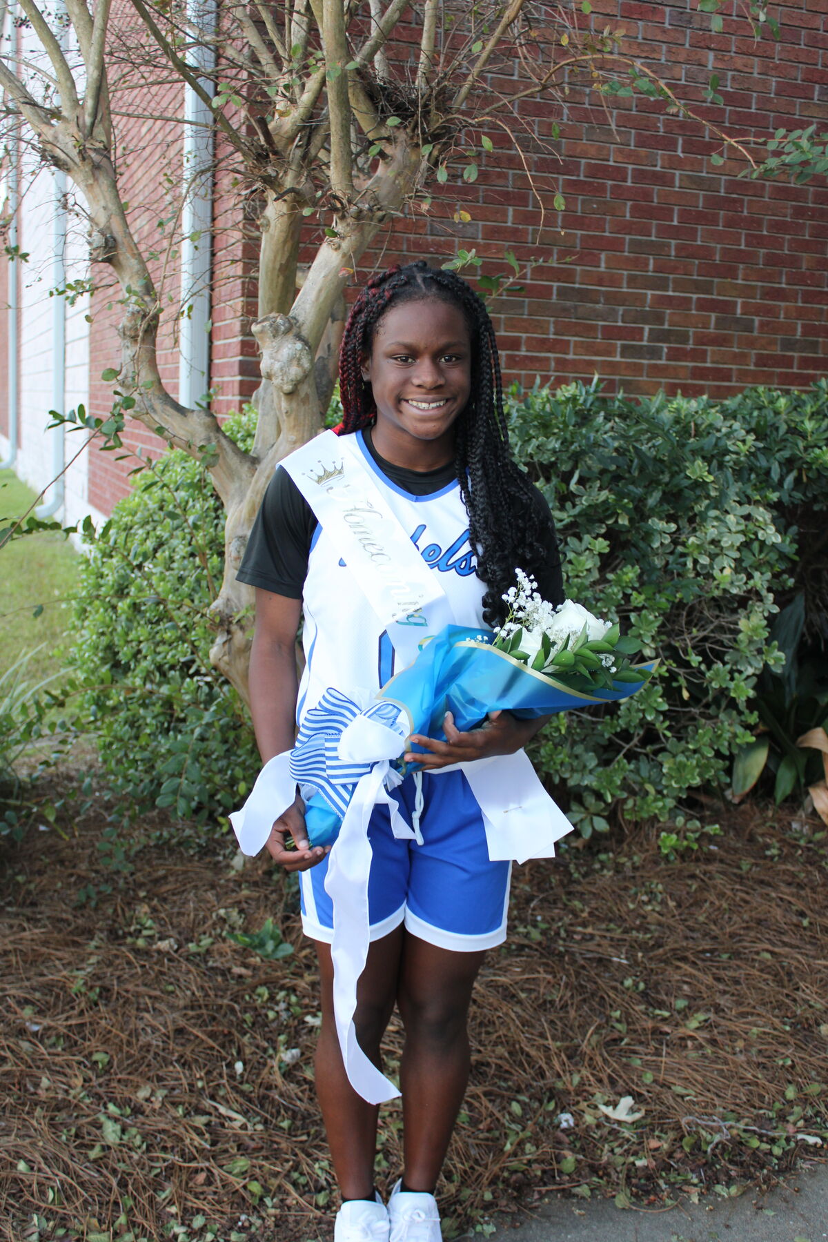 A smiling young woman in a blue and white sports uniform holding a bouquet of flowers.