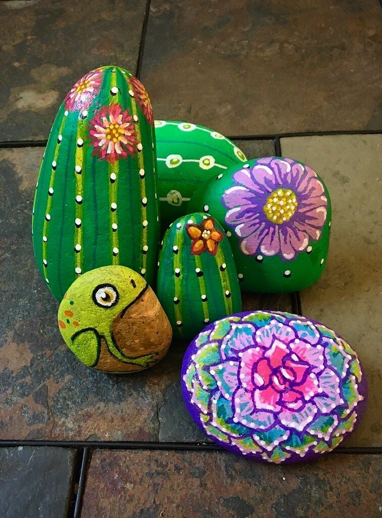 A collection of vibrantly painted rocks, featuring cactus designs with colorful flowers and a mandala pattern.
