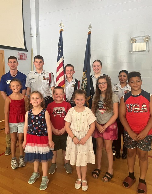 A group of young people and children stand together in front of two flags.