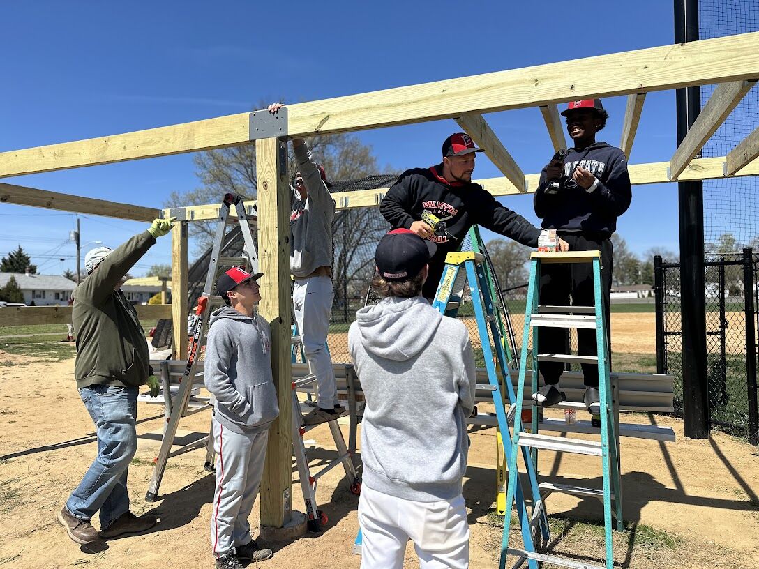 A group of people are constructing a wooden frame structure outdoors on a sunny day.