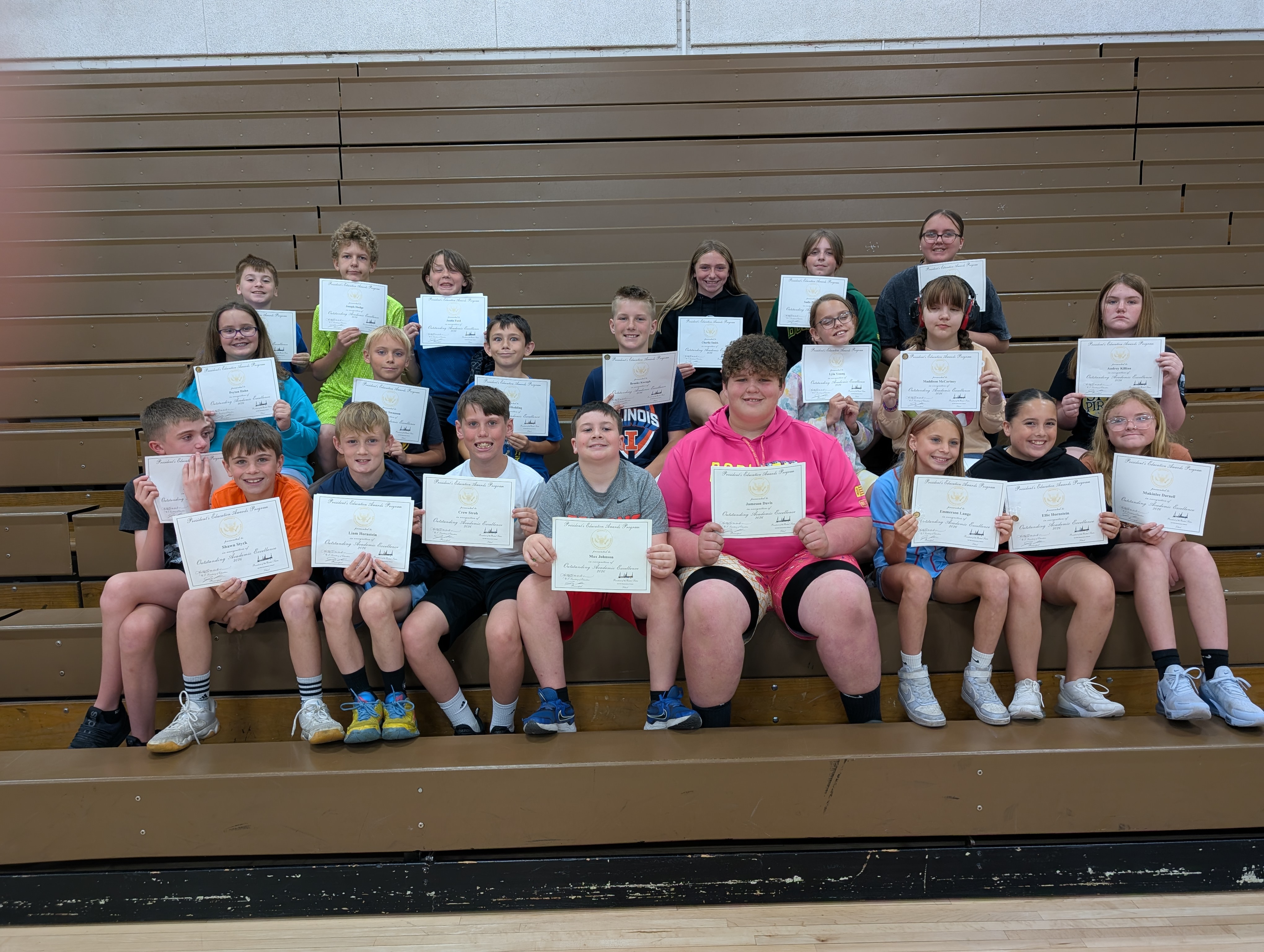 A group of students proudly hold certificates for outstanding academic excellence in a gymnasium.