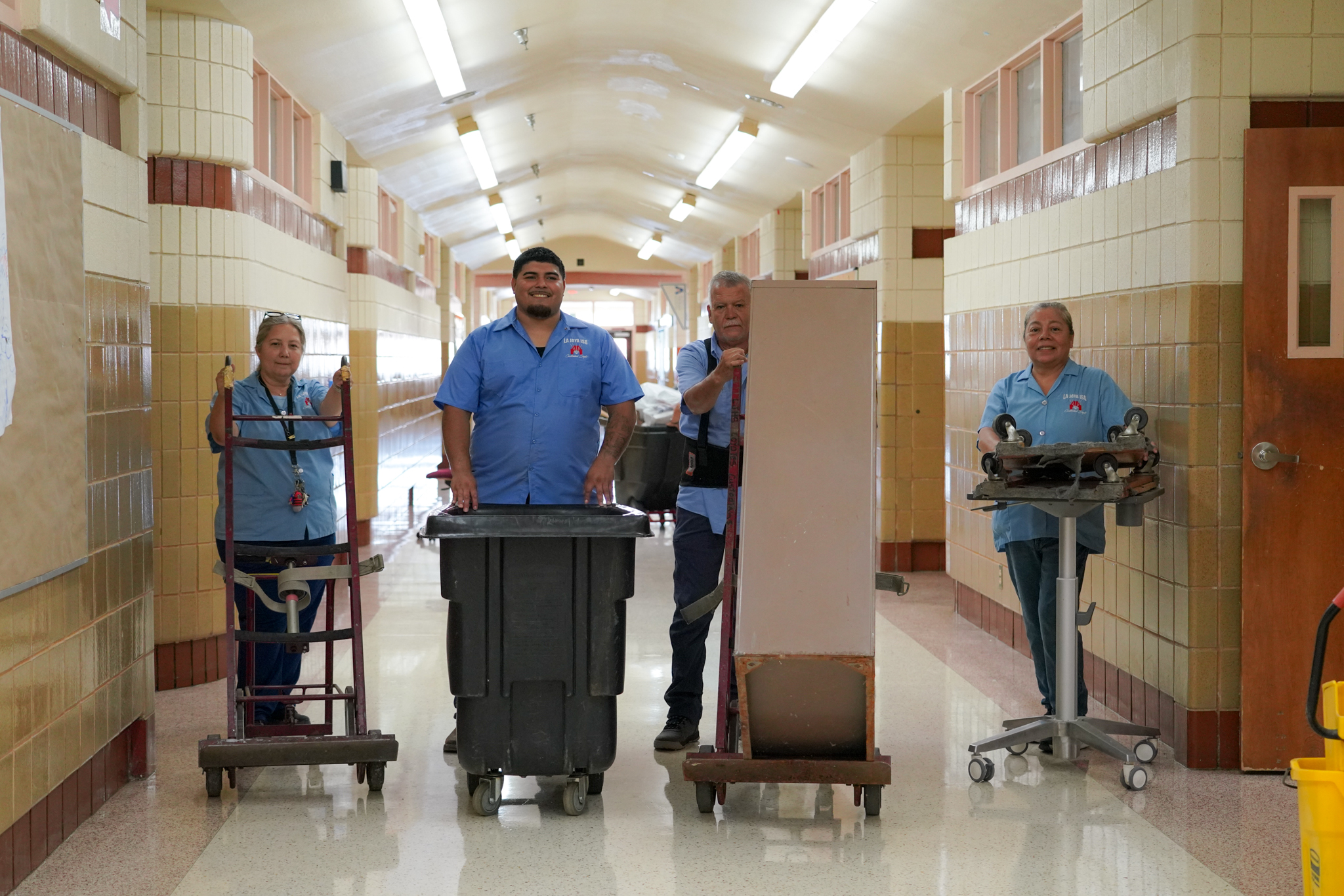 Four individuals in blue uniforms stand in a hallway with cleaning equipment.