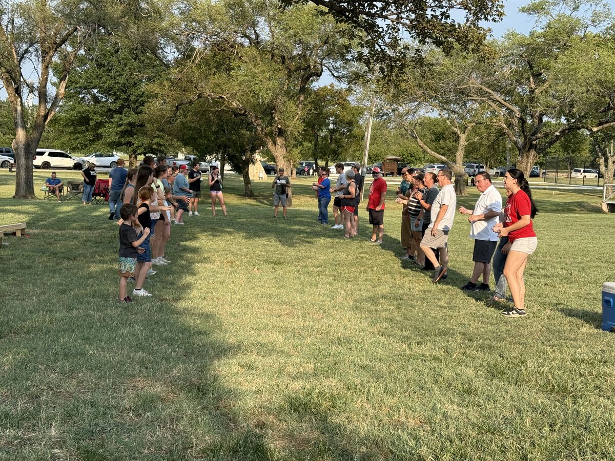 A group of people stand in two lines facing each other on a grassy field, possibly for a game or activity.