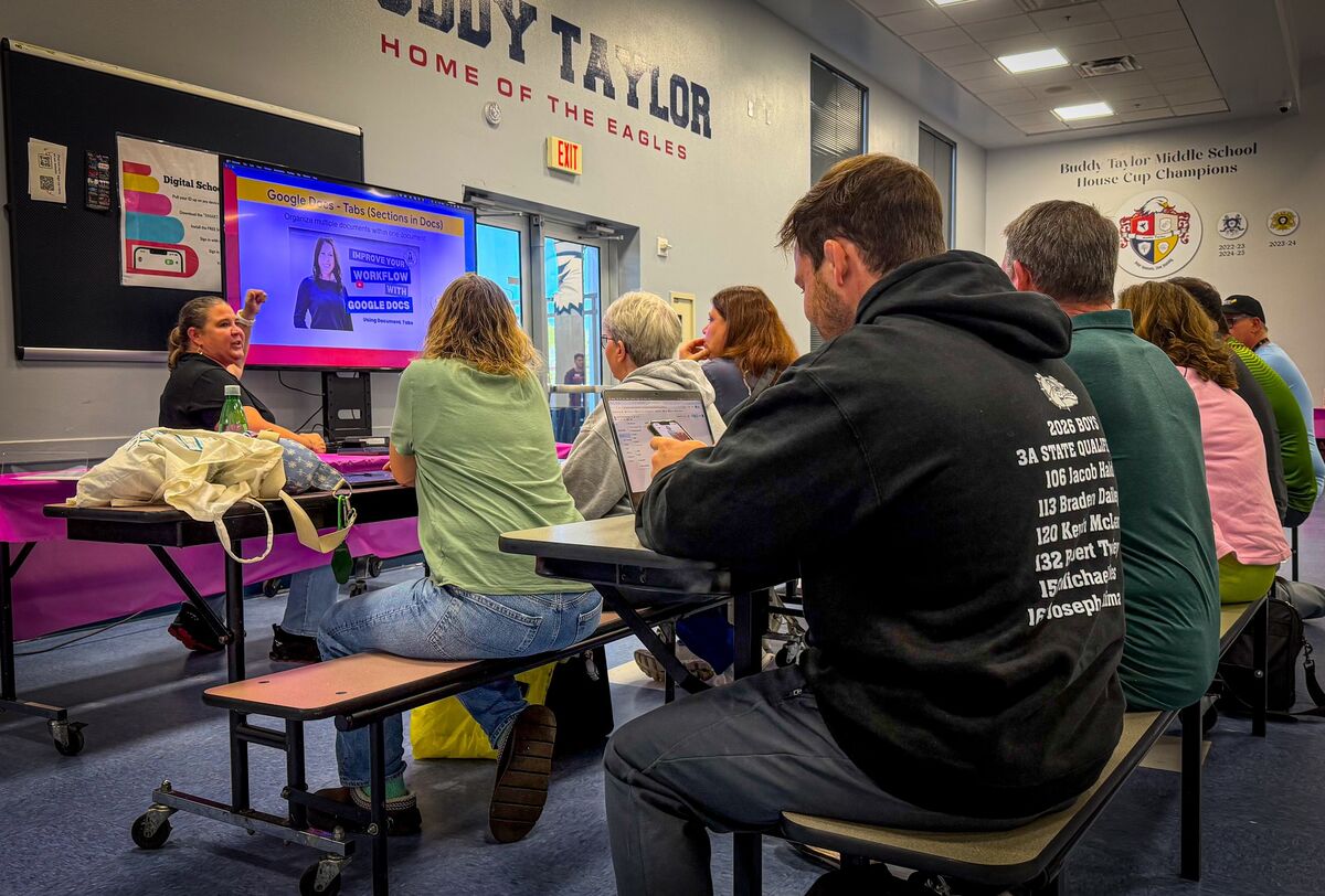 A presenter gestures towards a large screen displaying a tutorial on Google Docs tabs, while an audience watches.