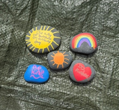 Five painted rocks with positive messages and colorful designs are arranged on a textured surface.