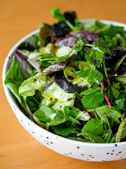 A close-up of a fresh salad with mixed greens and a balsamic vinaigrette in a speckled white bowl.