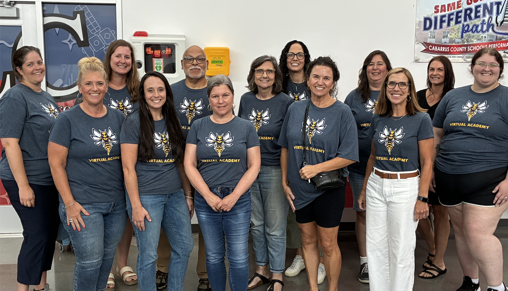 A group of adults wearing matching dark blue t-shirts with a bee logo and the text 'VIRTUAL ACADEMY' stand together.