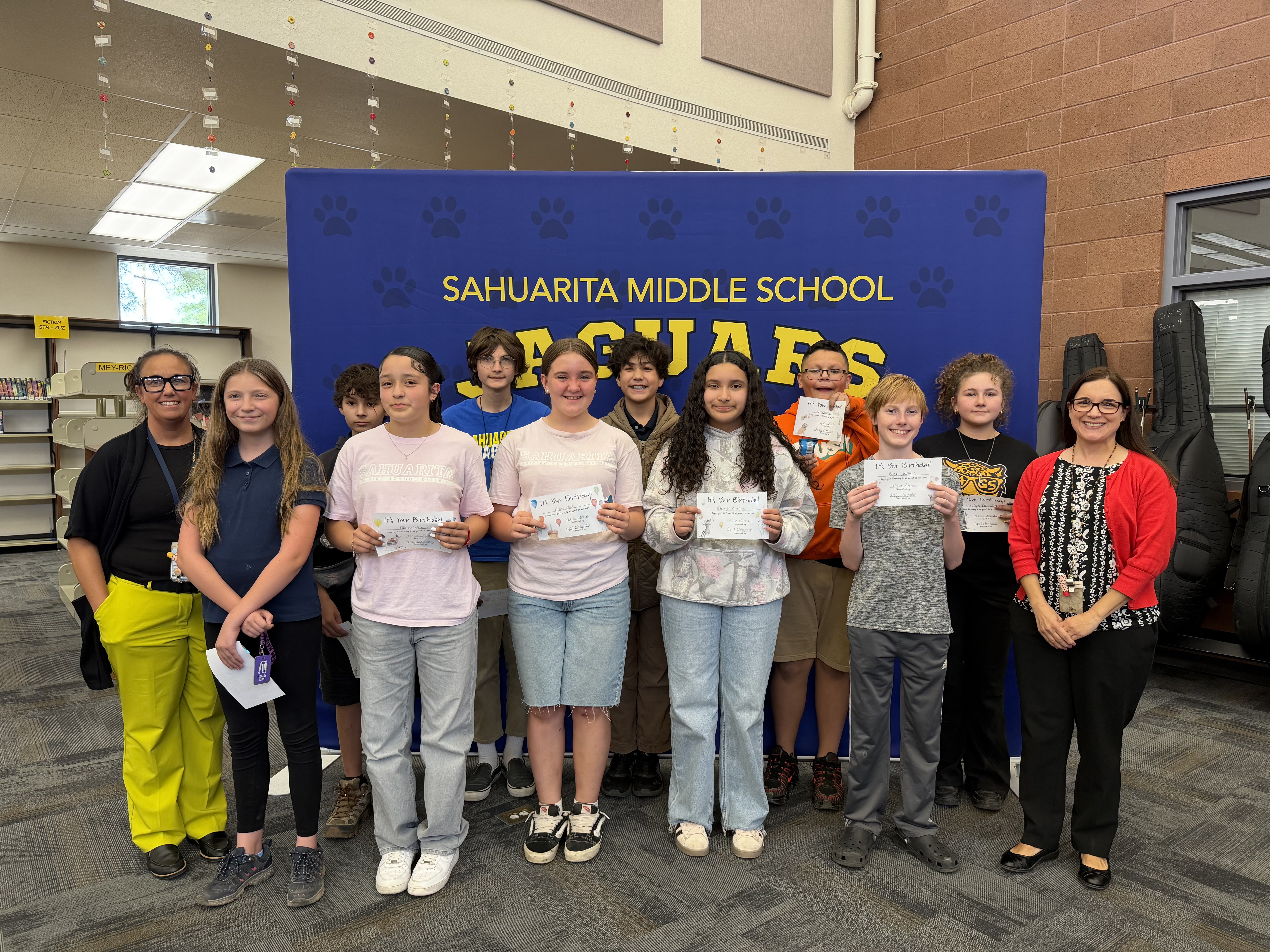 Students and teachers pose for a photo in front of a banner.