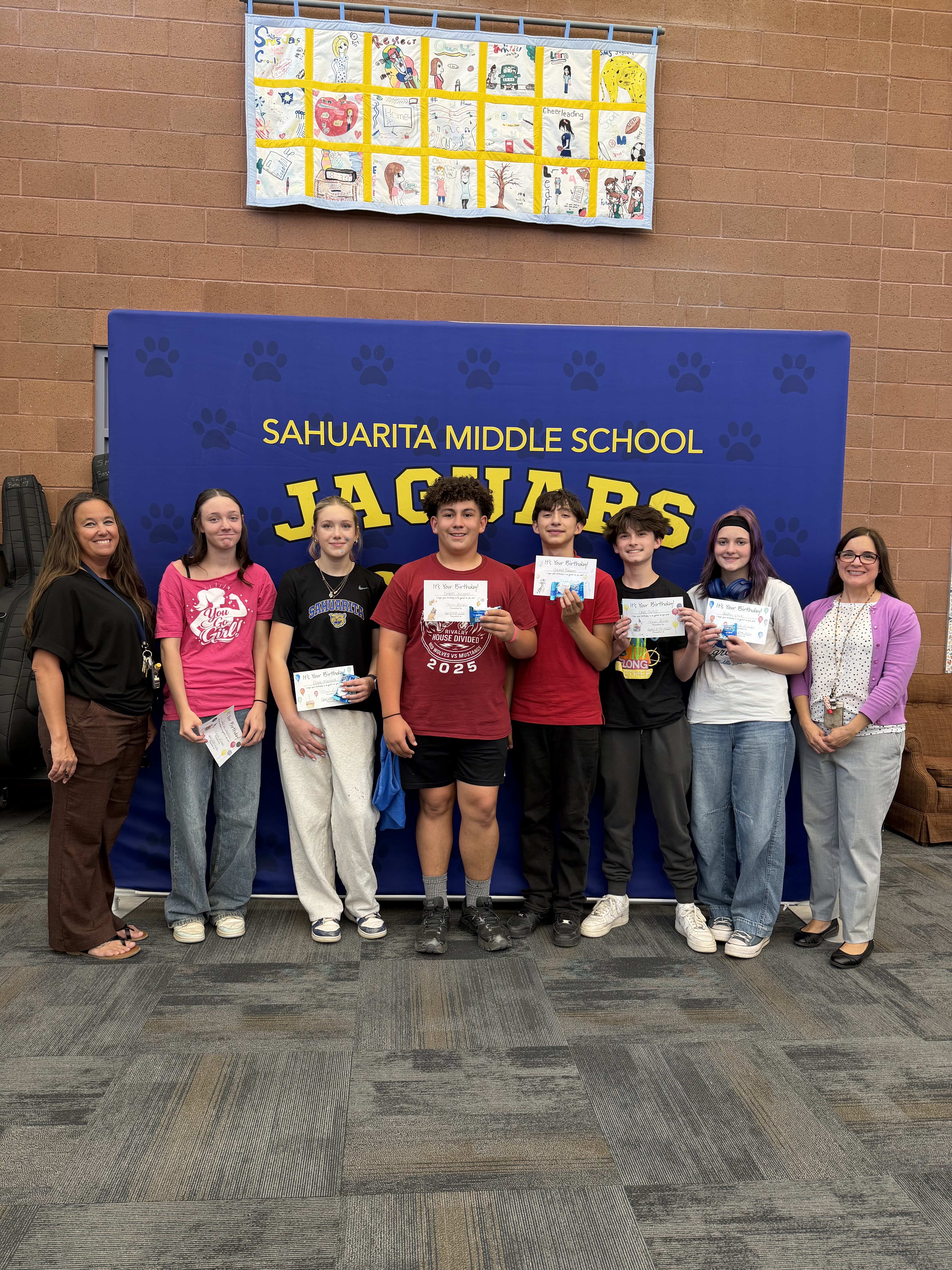 Students and teachers pose for a photo in front of a banner.