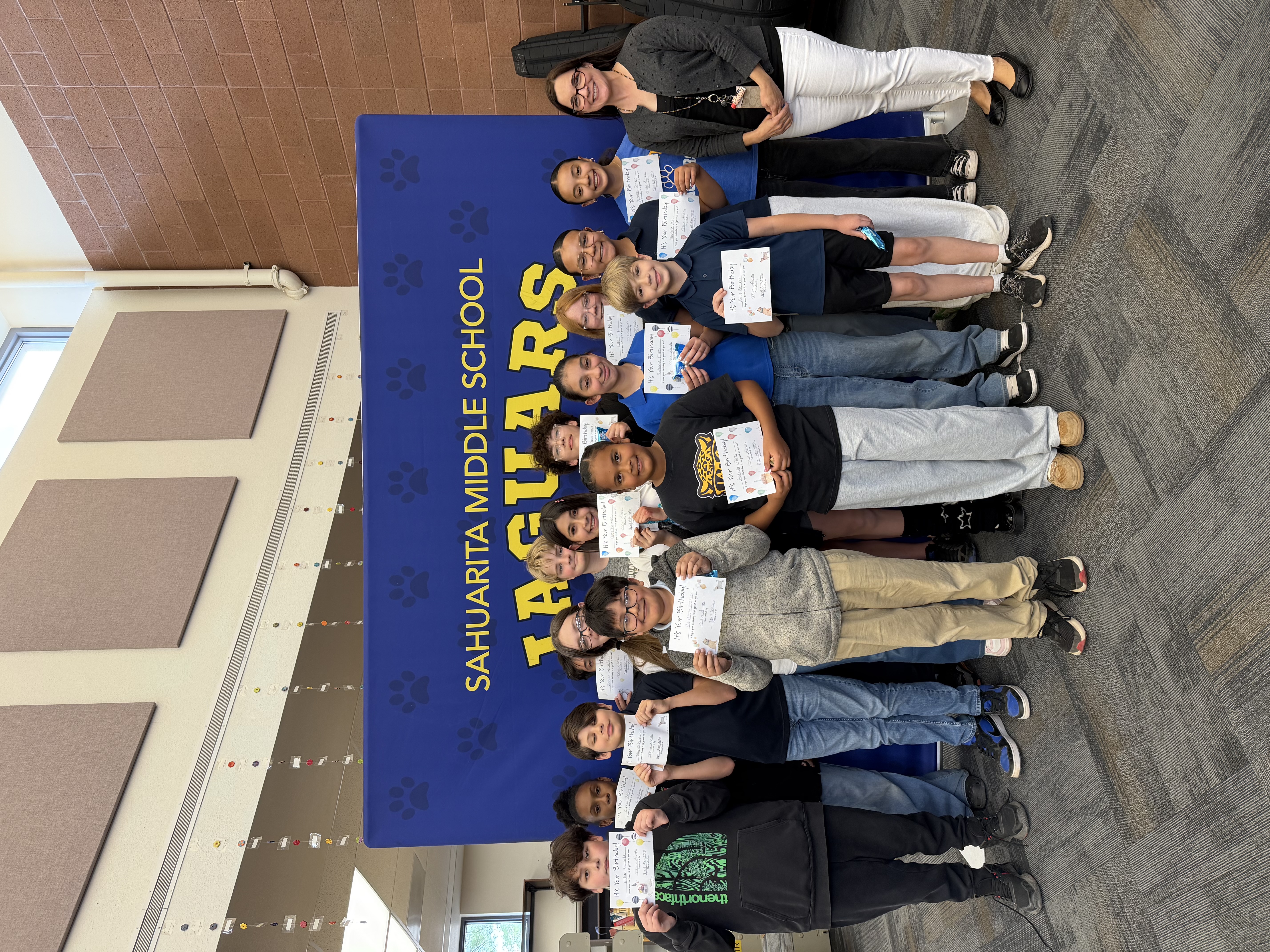 A group of students and a teacher pose for a photo in front of a banner.