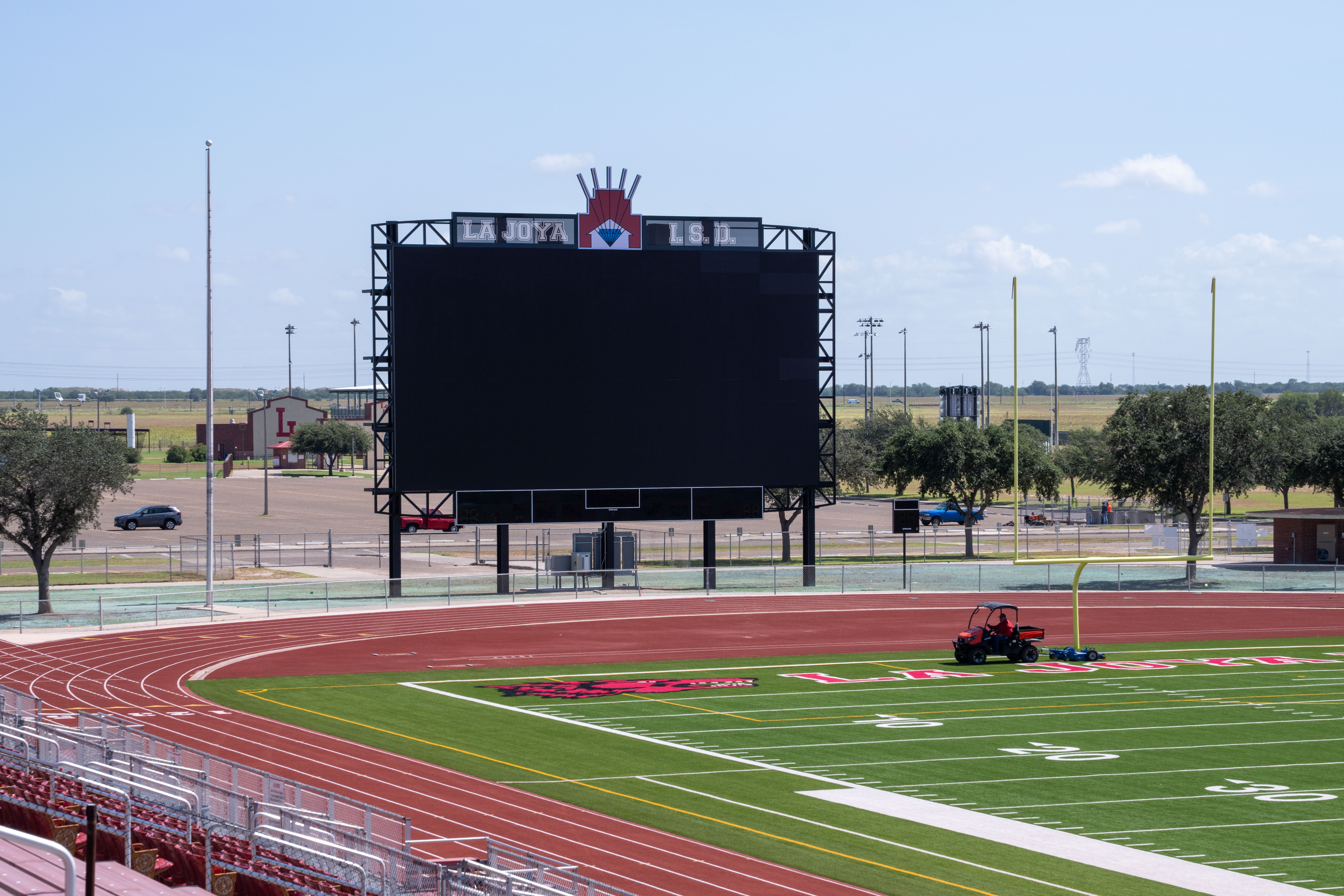 A large black scoreboard with 'LA JOYA L.S.D.' text stands over an empty football field.