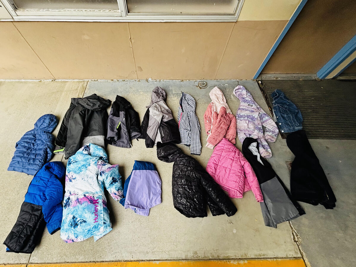 A collection of children's jackets and coats are laid out on a concrete surface.