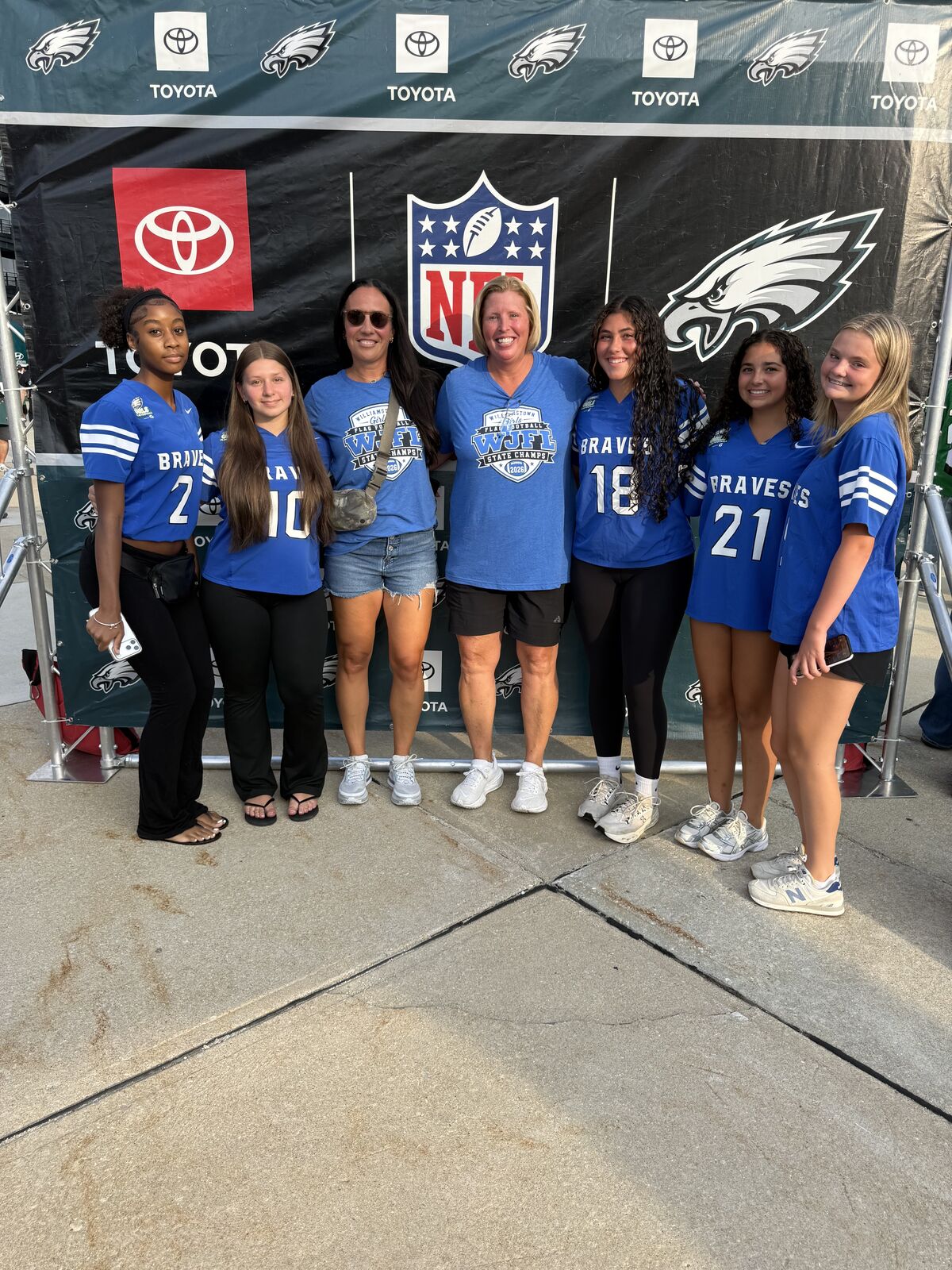 A group of women and girls in blue jerseys pose for a photo in front of a banner with the Philadelphia Eagles logo and Toyota branding.