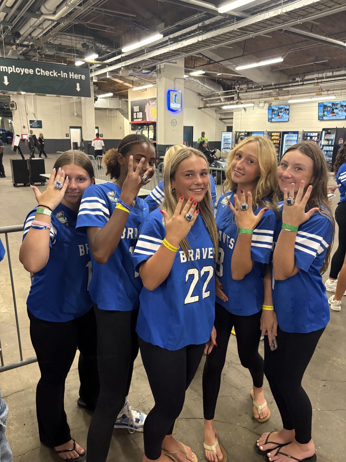 Four young women in blue jerseys proudly display championship rings.