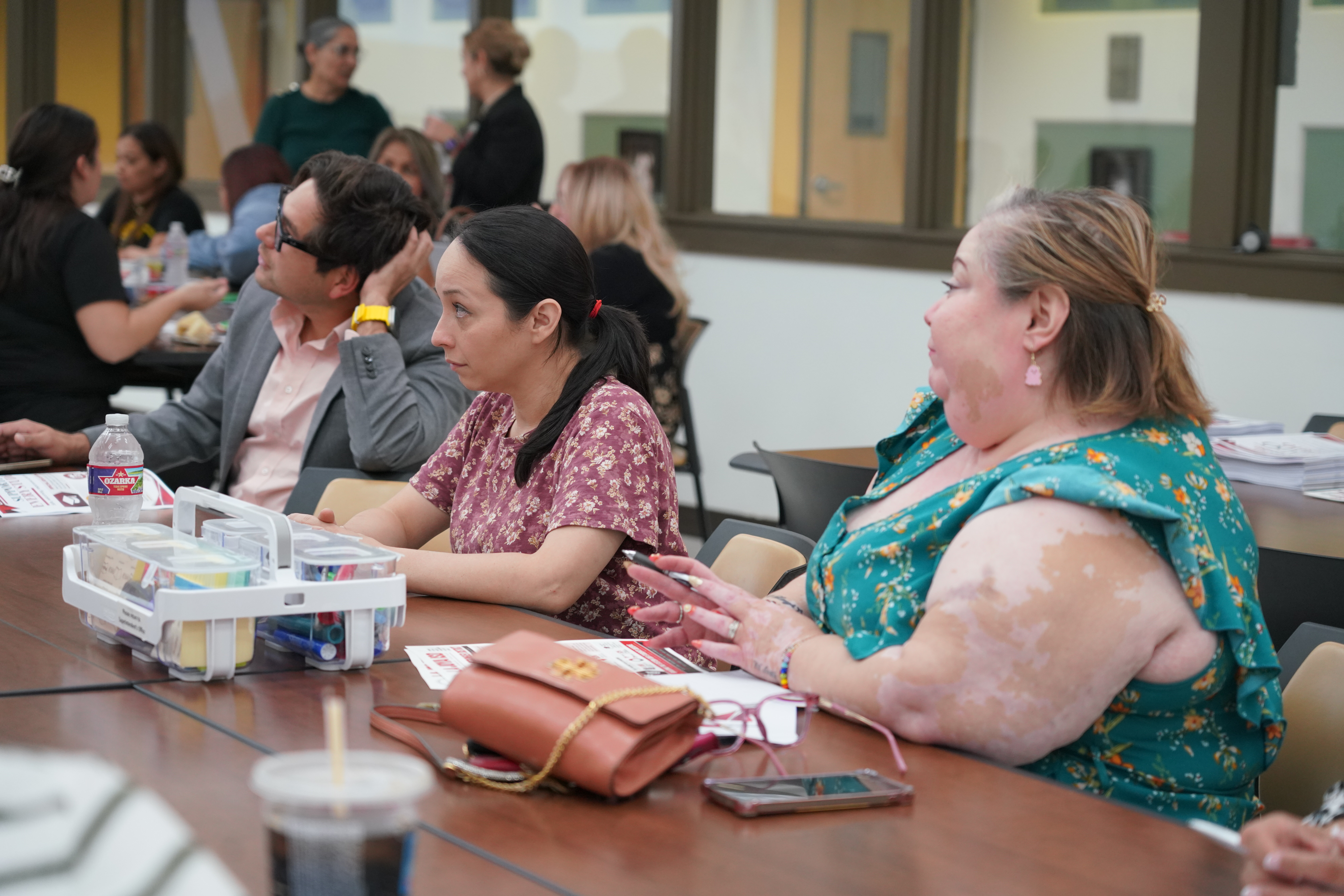 Attendees seated at tables in a brightly lit room, listening attentively during a presentation.