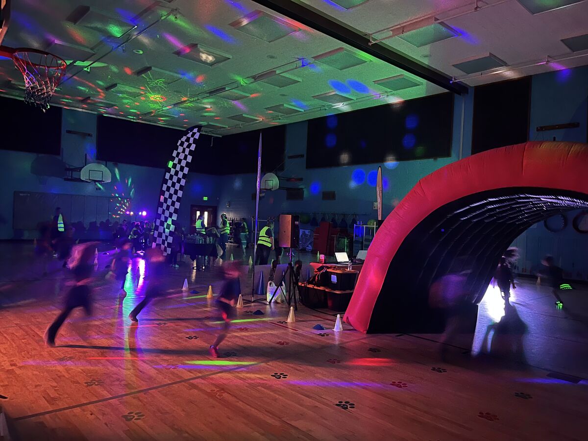 Children run through a gym decorated with colorful lights and an inflatable archway.