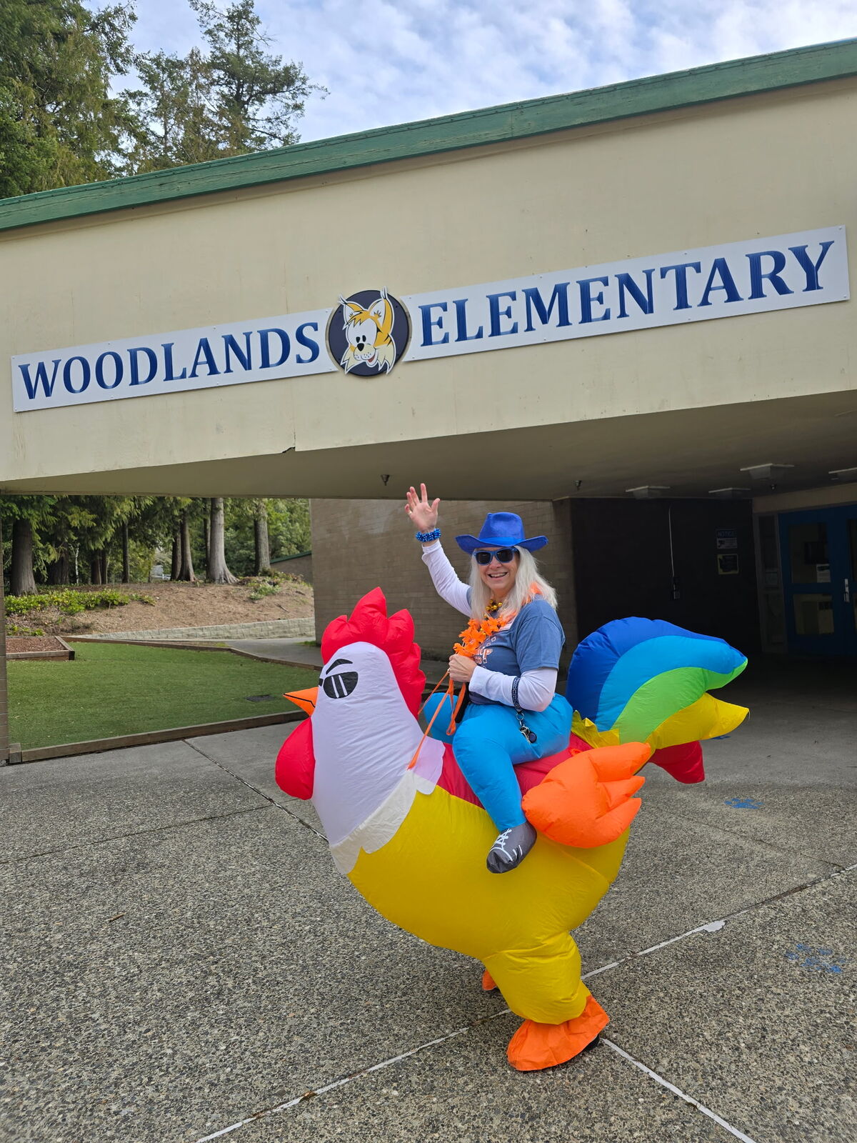 A person in a colorful inflatable chicken costume waves in front of Woodlands Elementary.