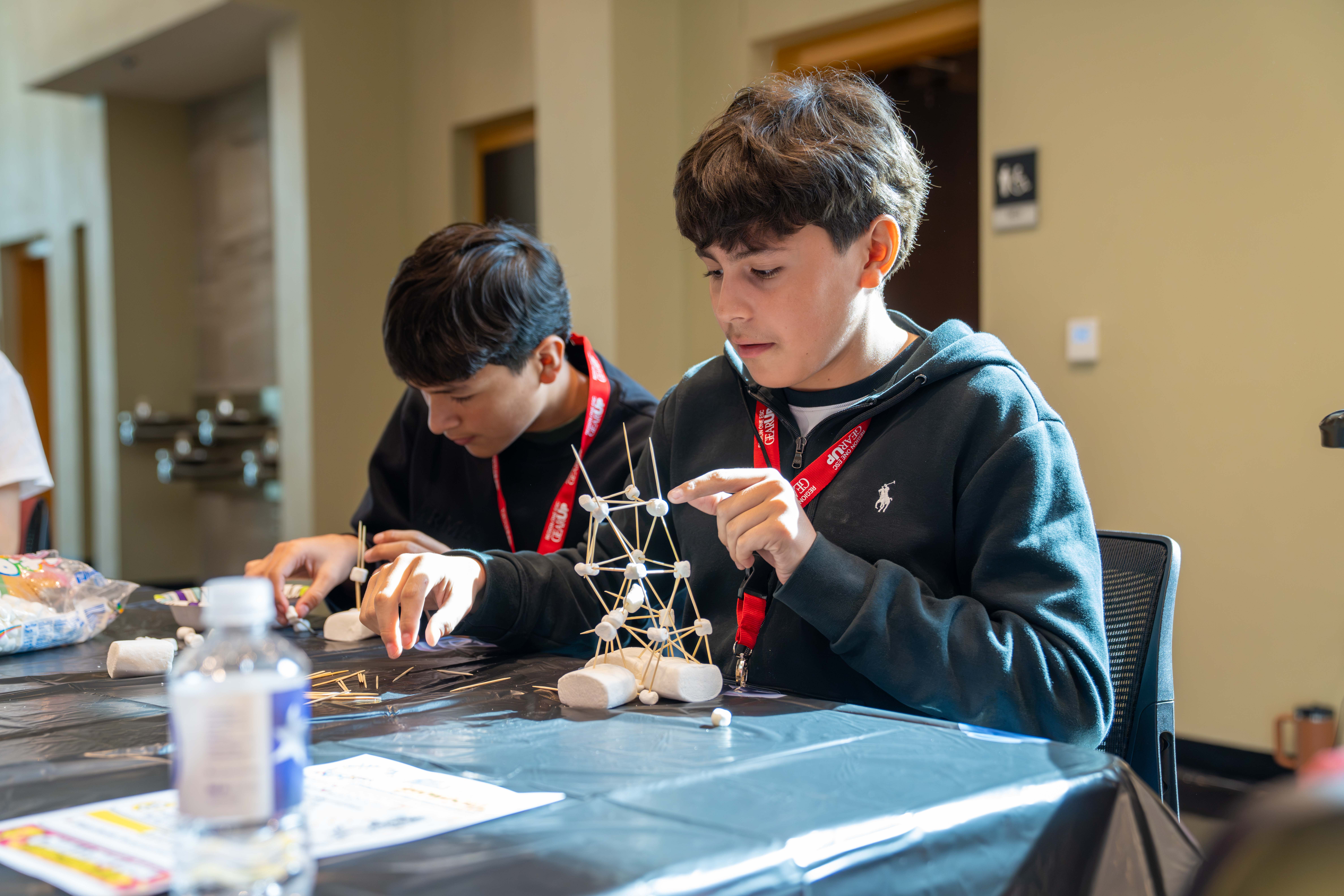 Two students build a tower structure using toothpicks and marshmallows during a classroom activity.