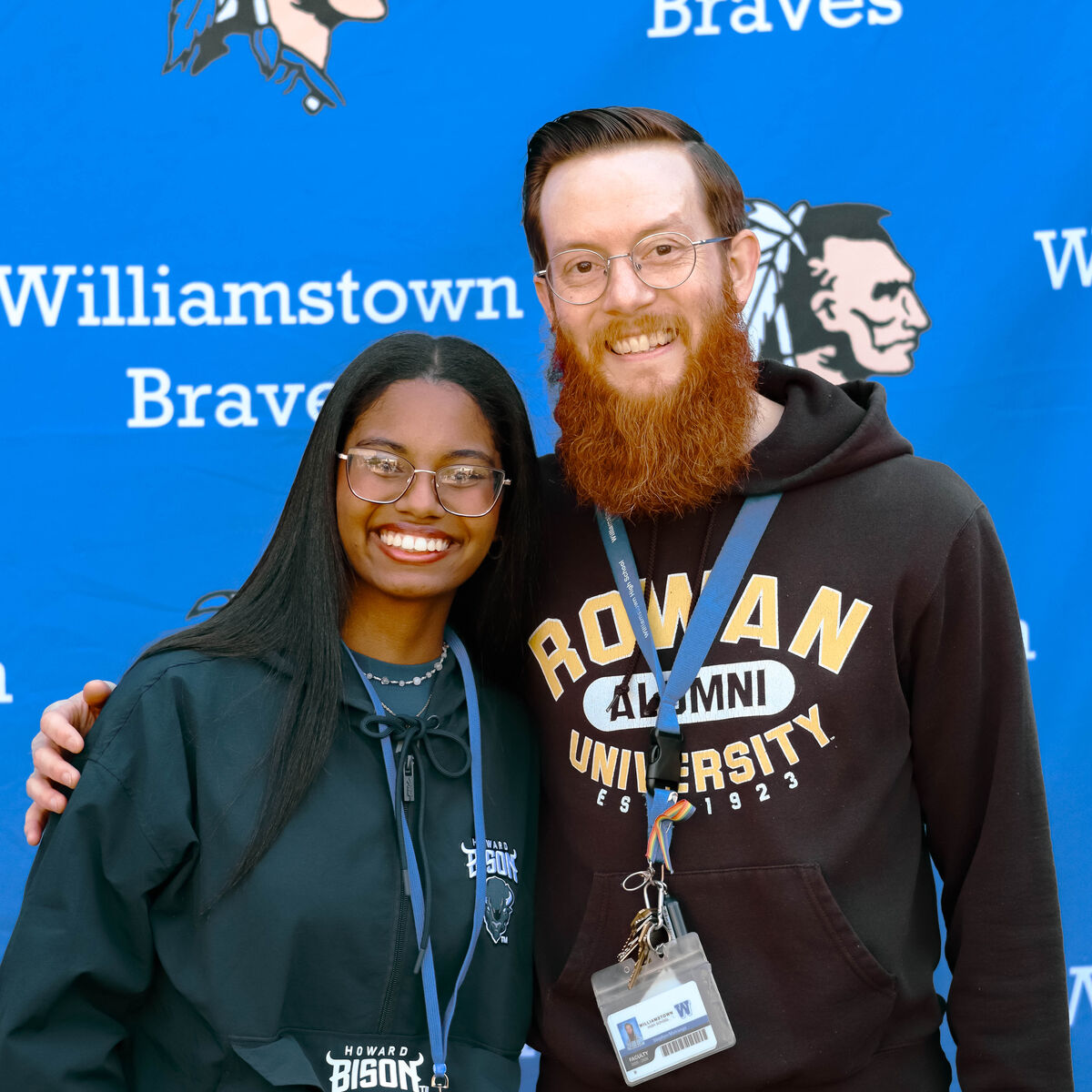 A young woman and a man with a beard smile at the camera in front of a blue banner with "Williamstown Braves" text.