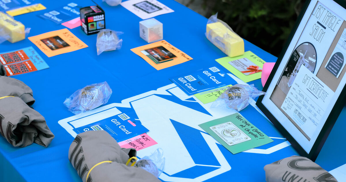 A blue tablecloth displays various gift cards, promotional flyers, and wrapped items, including a framed gift certificate for 'Last Tangle Salon'.