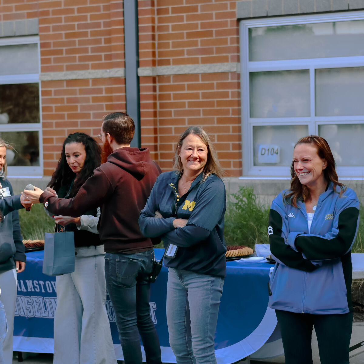 People stand near a table with a blue tablecloth, some smiling and interacting.
