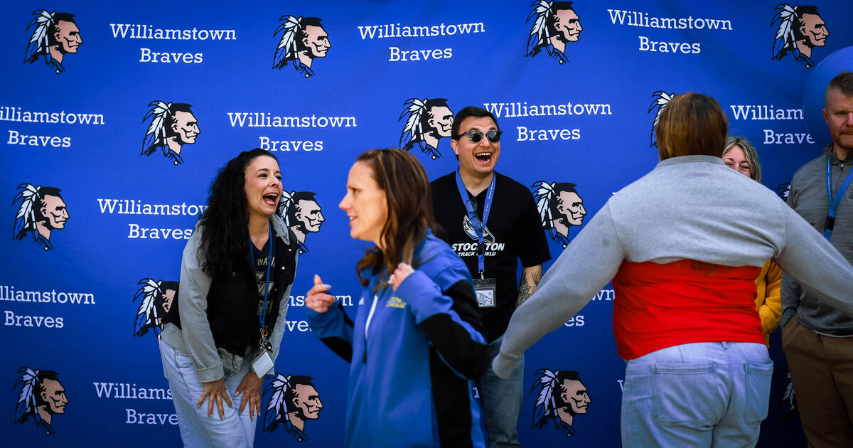 People laugh and interact in front of a blue backdrop with repeated "Williamstown Braves" logos and imagery.