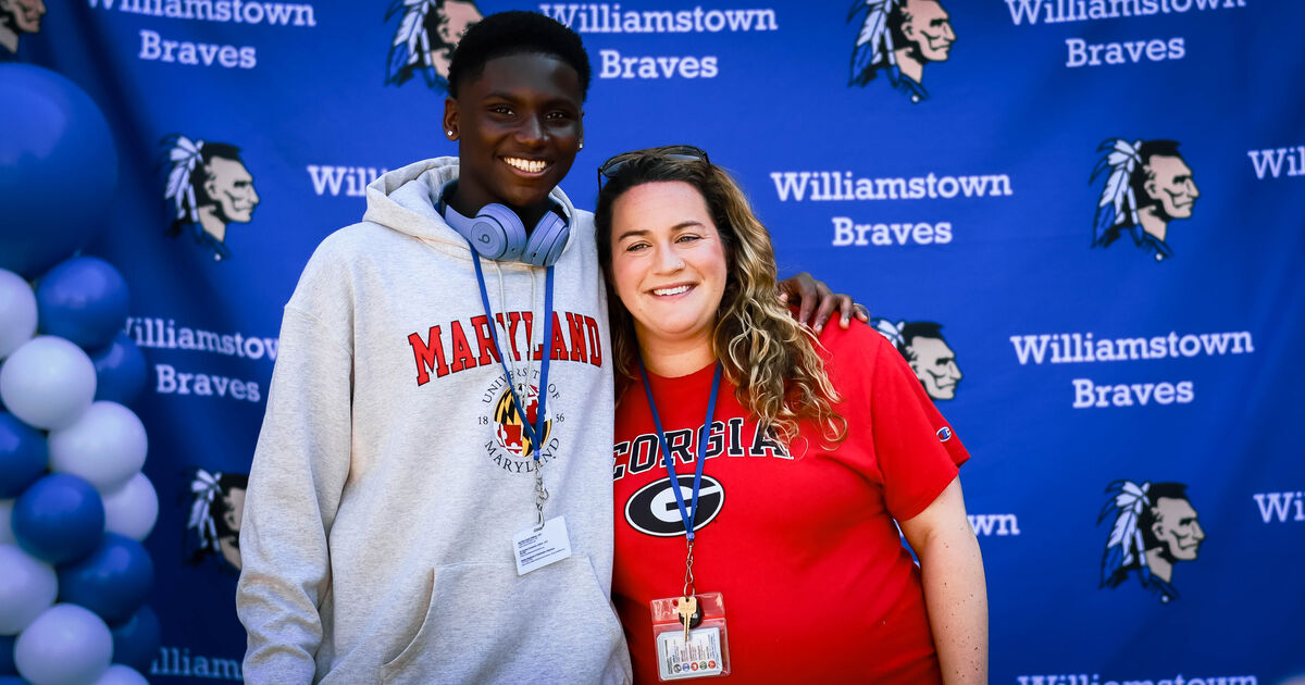 A young person wearing a Maryland hoodie and headphones stands with an adult wearing a Georgia t-shirt, both smiling.