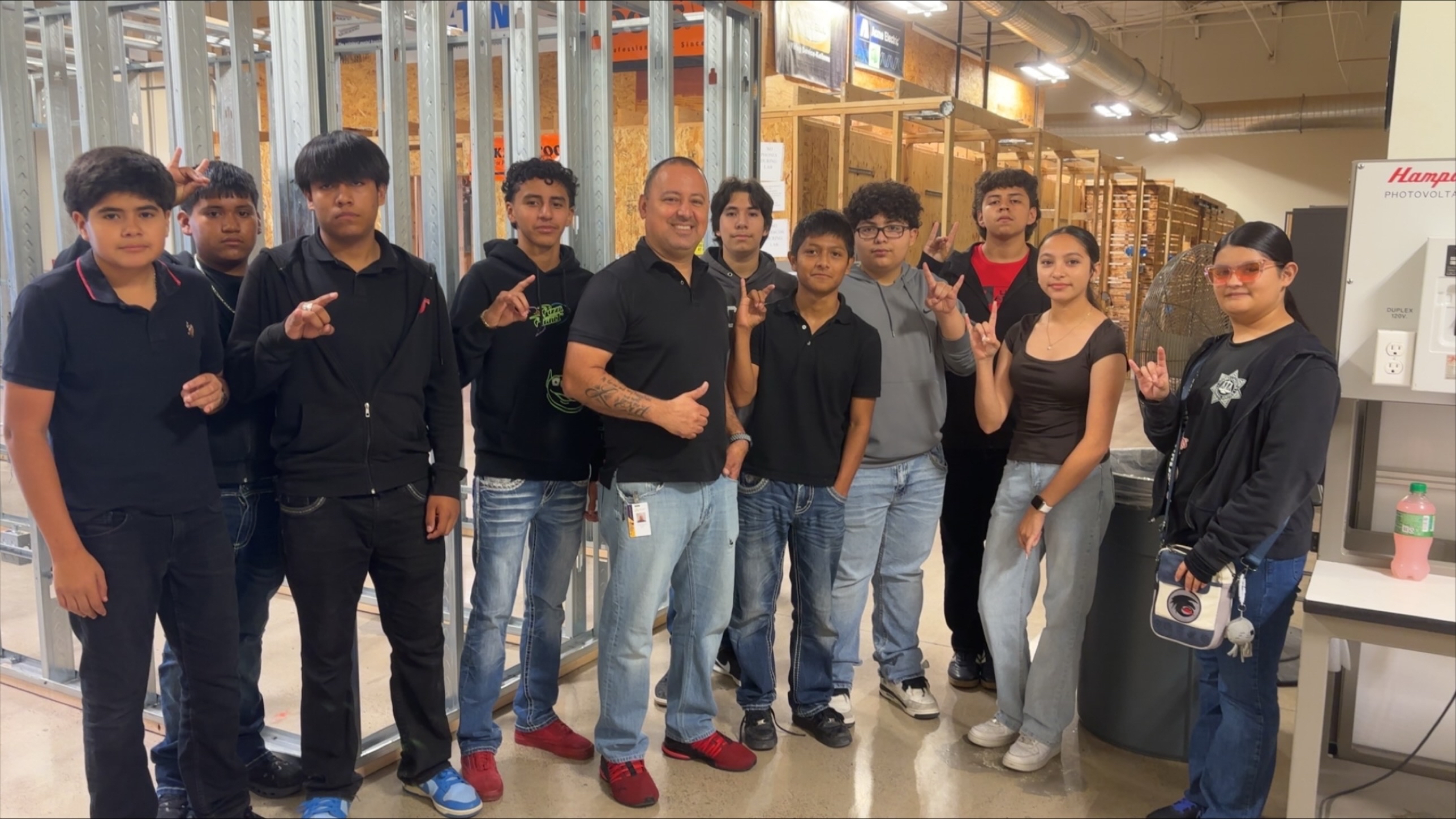 A group of young people and an adult man pose for a photo in a workshop setting.