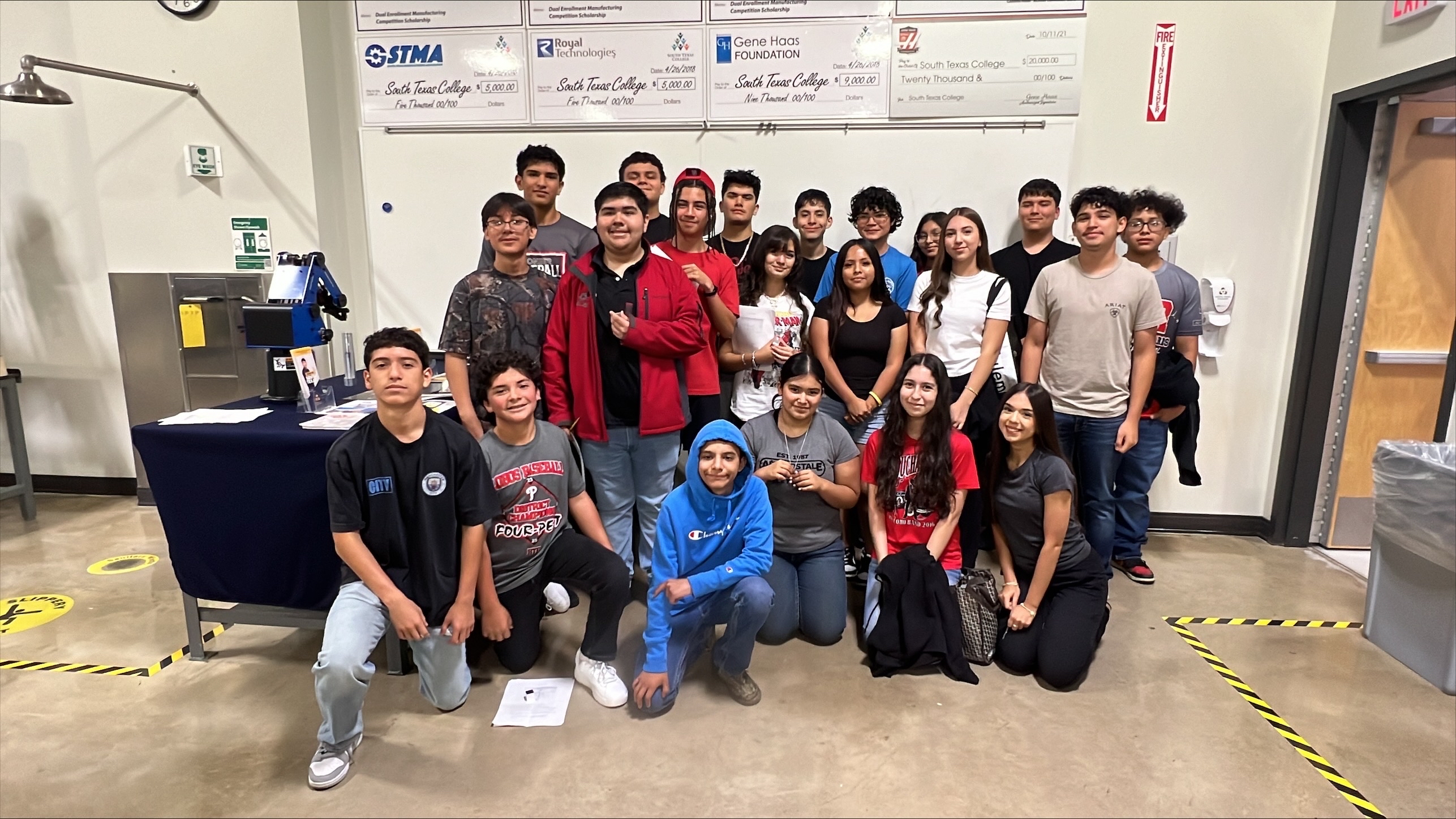 A diverse group of students poses for a photo in a classroom or workshop setting.