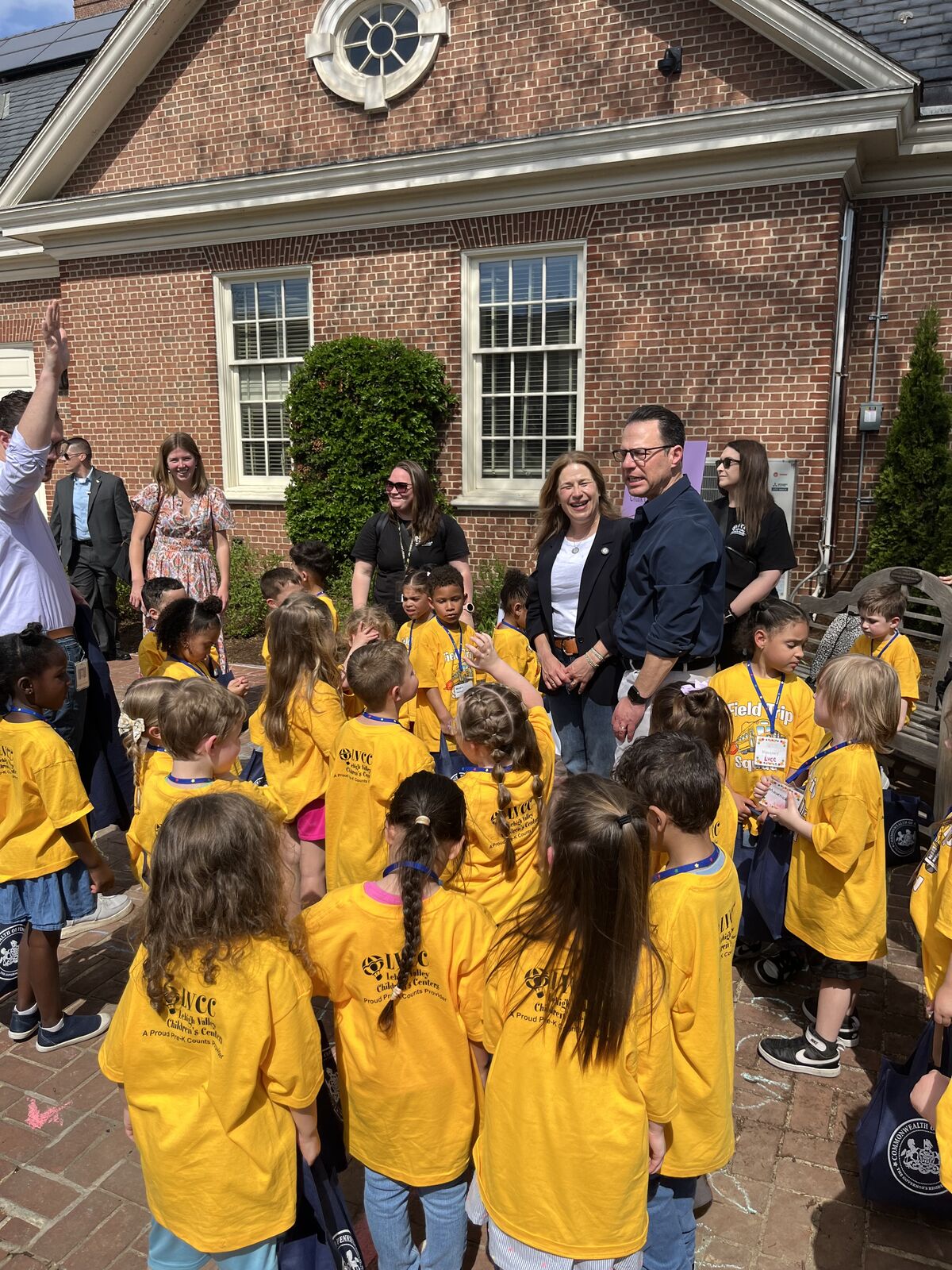 A group of children in bright yellow t-shirts gather outdoors with adults.