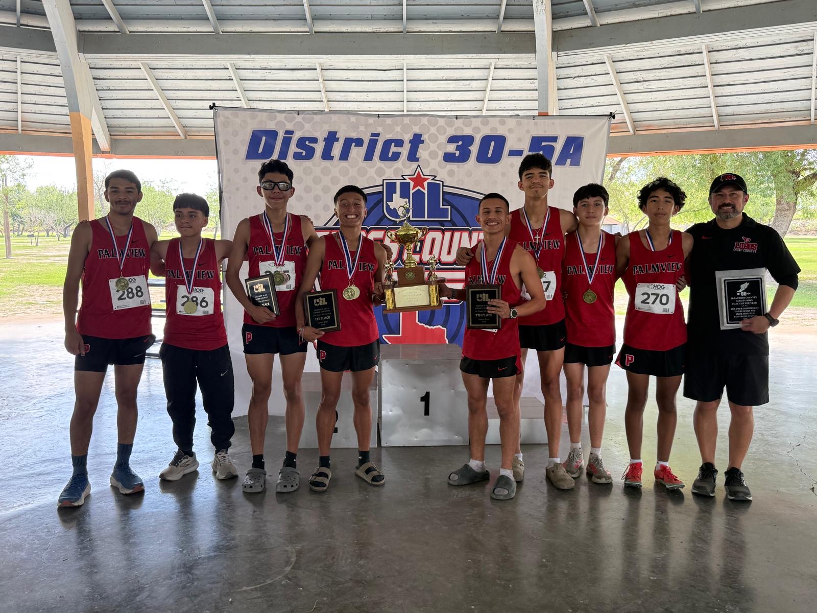 A high school cross country team in red uniforms poses proudly with their trophies and medals under a pavilion.