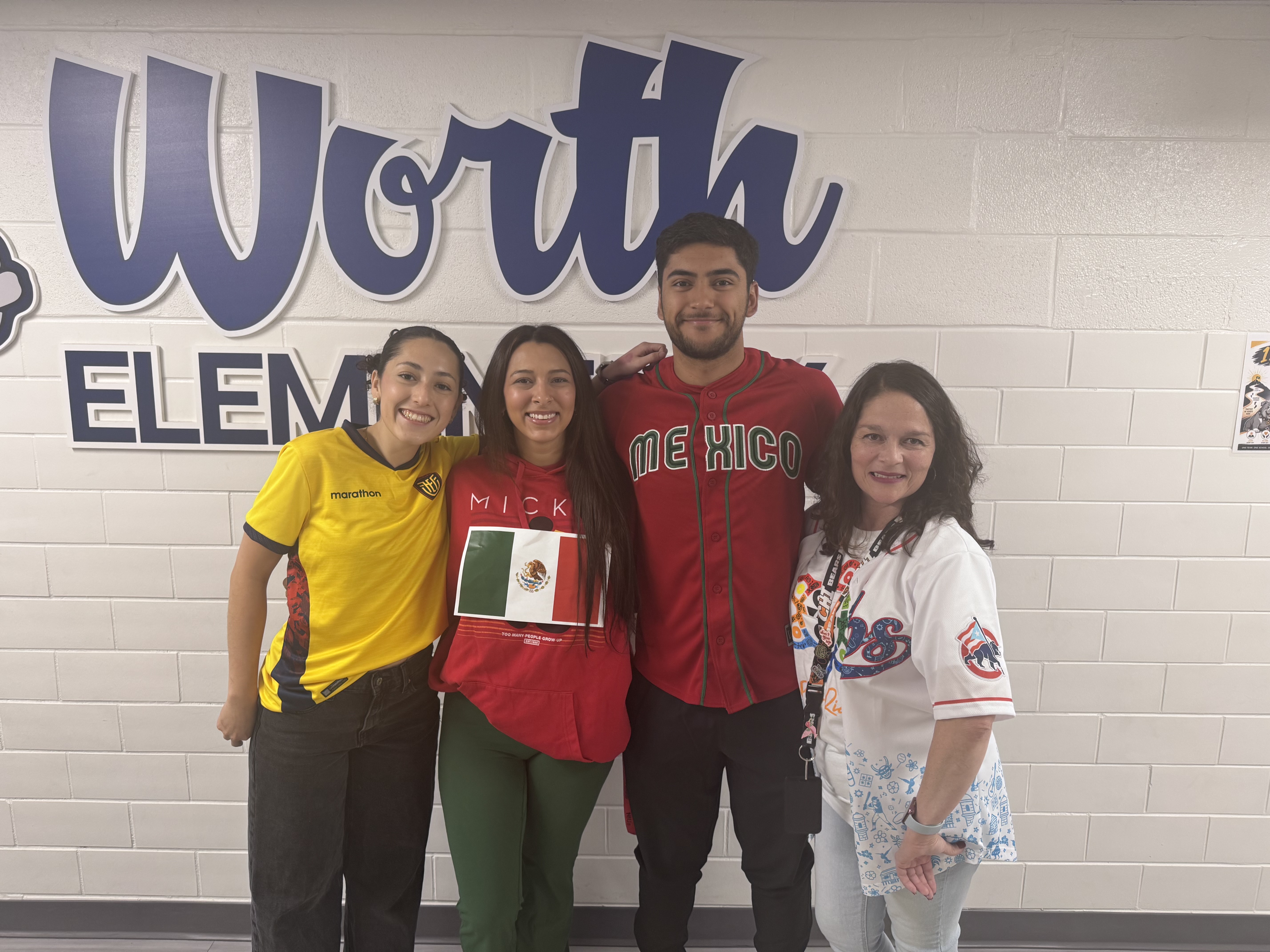 Four people smile together inside Worth Elementary, standing in front of a blue and white brick wall.