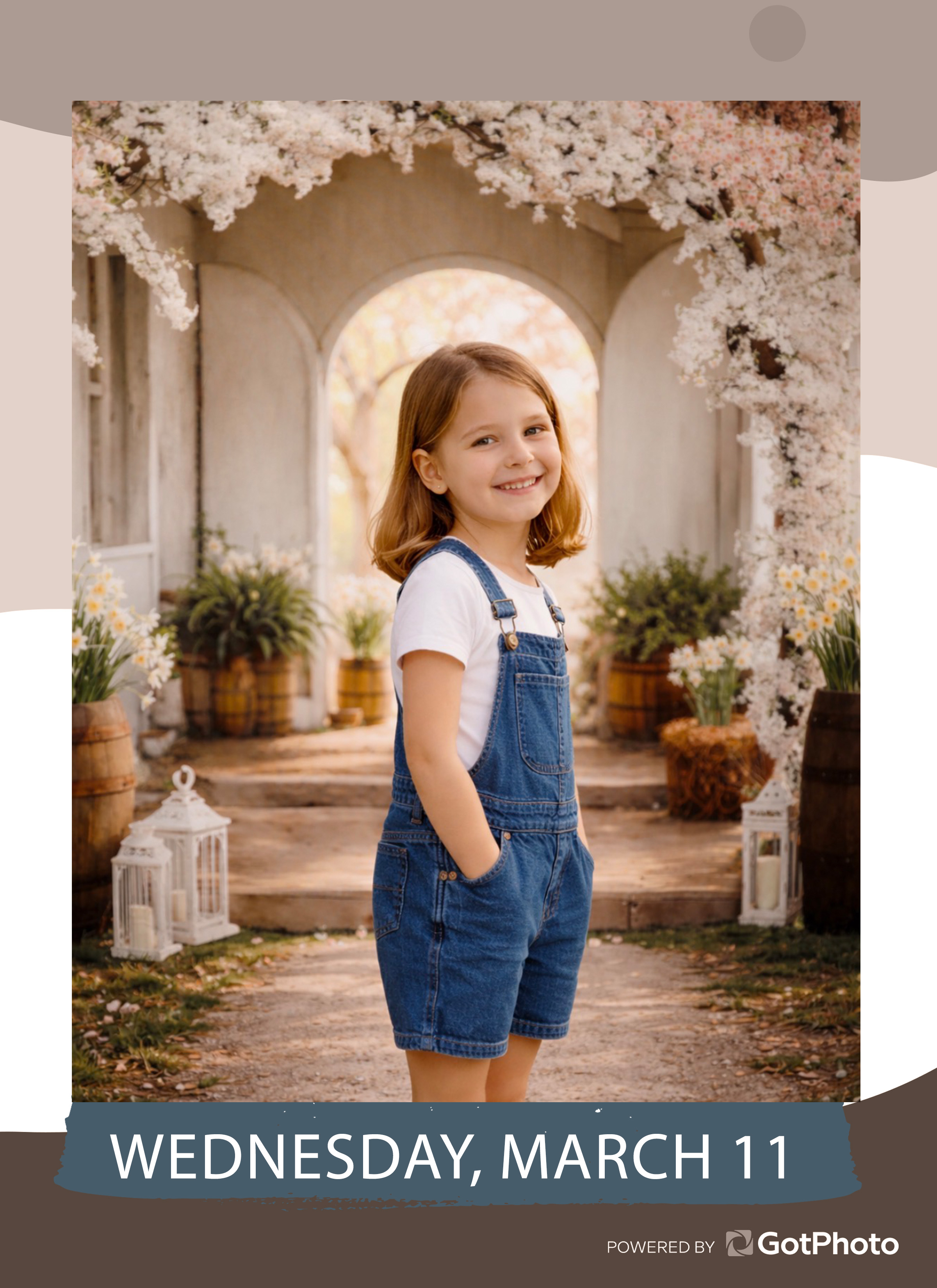 A young girl in denim overalls smiles at the camera in a garden setting with blooming trees.