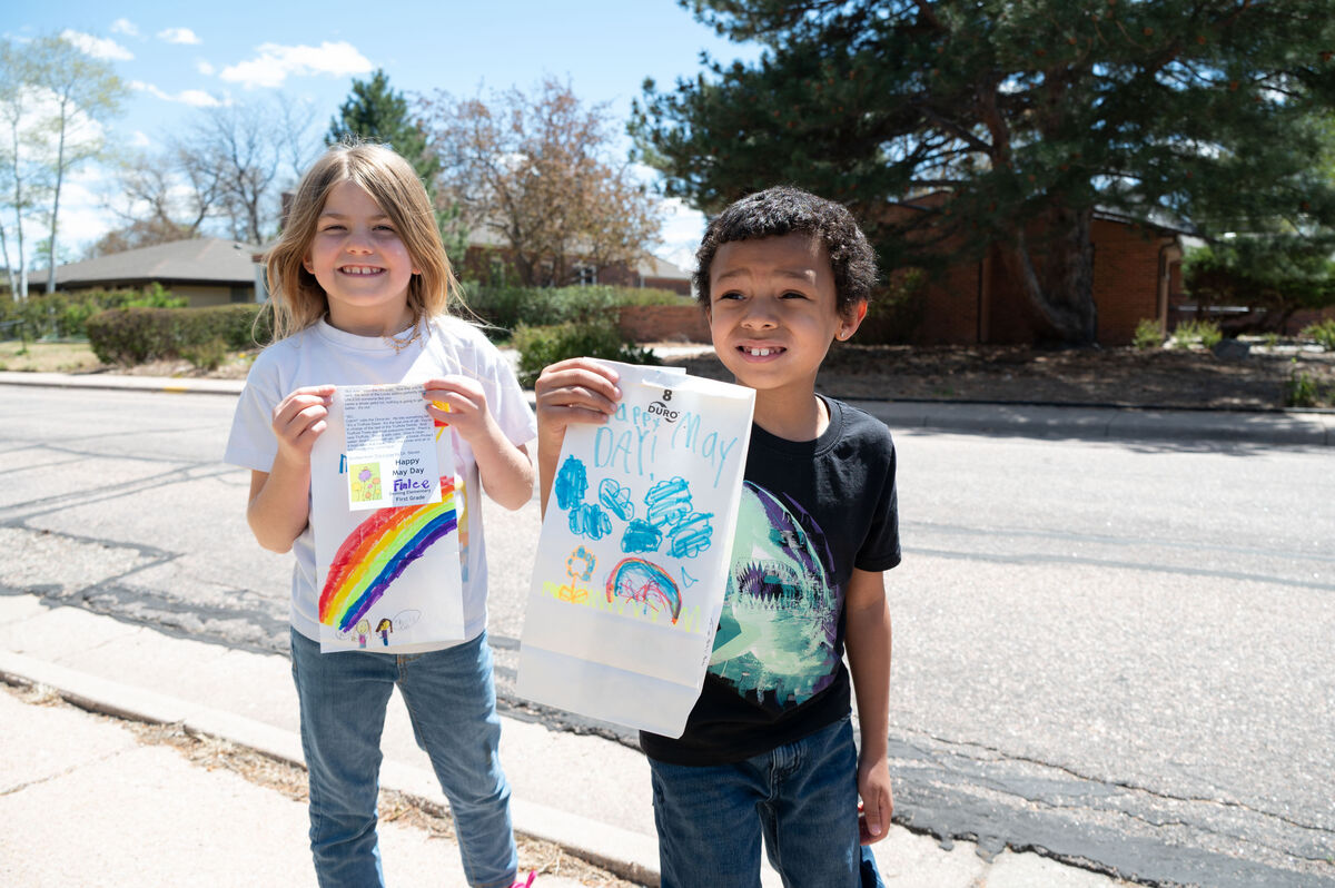 Two smiling children hold up decorated bags, one with a rainbow and figures, the other with blue drawings.