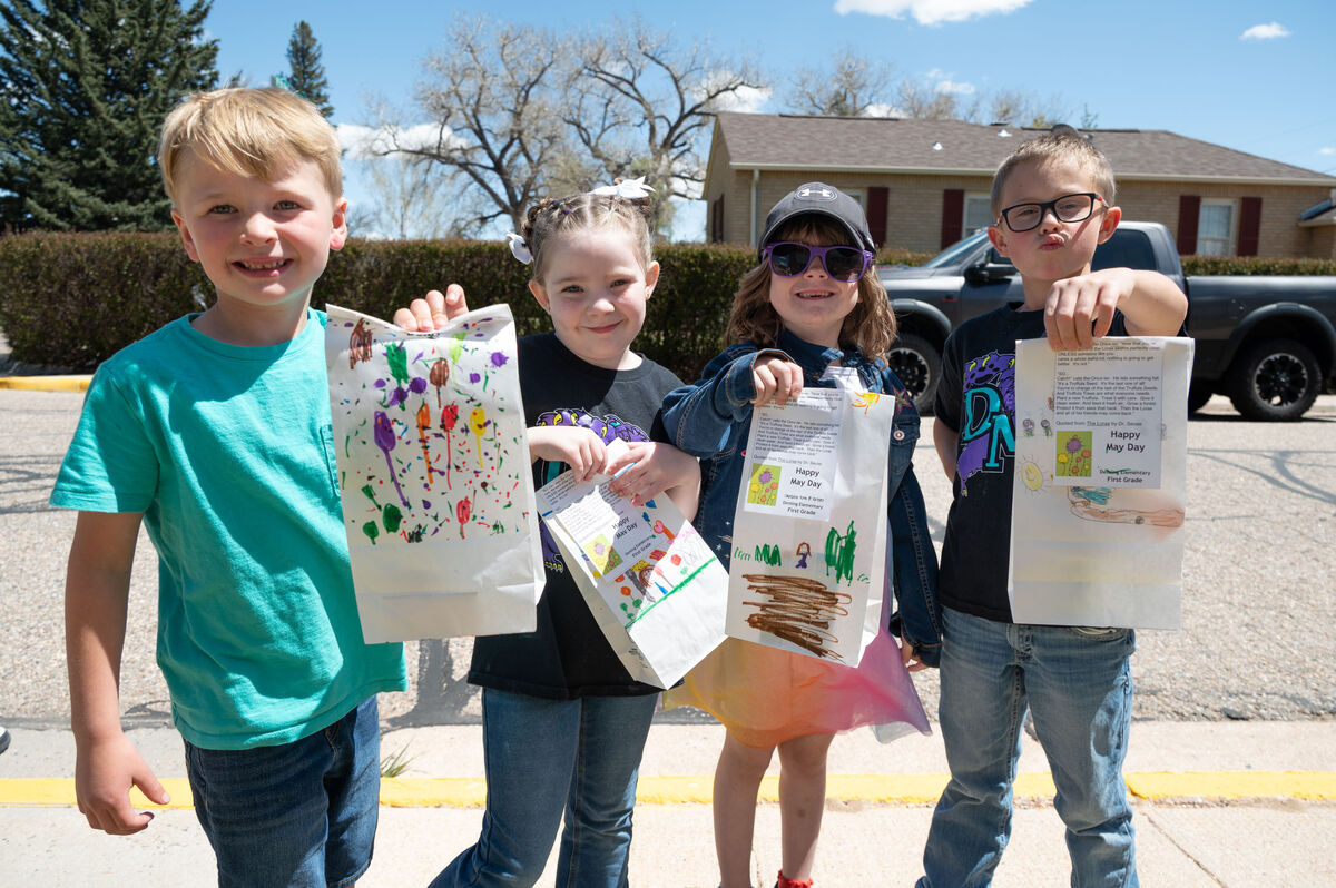 Four children proudly display decorated paper bags with drawings and text, including "Happy May Day" and quotes from Dr. Seuss.