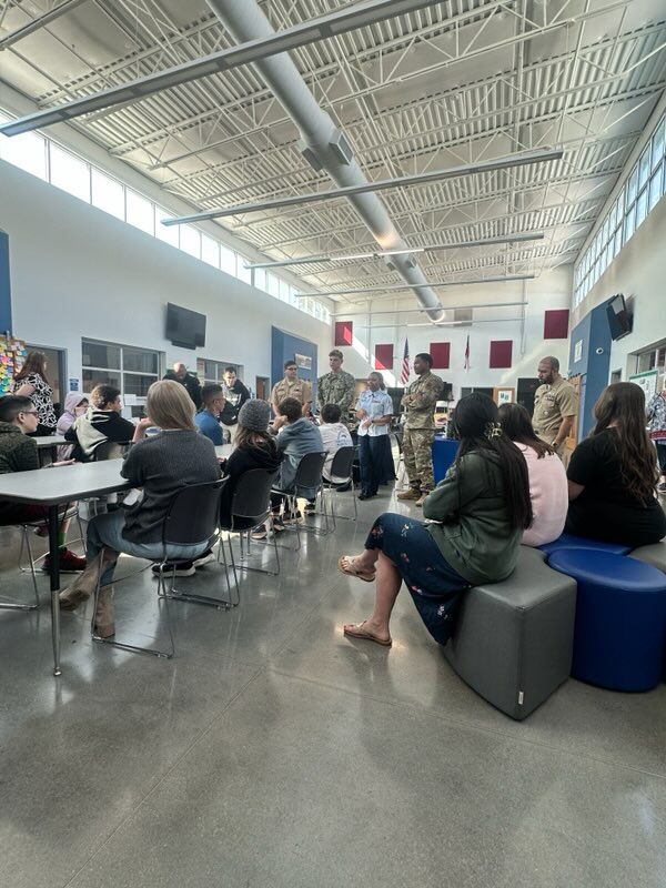 Military personnel stand and address a group of seated students in a bright, modern room.