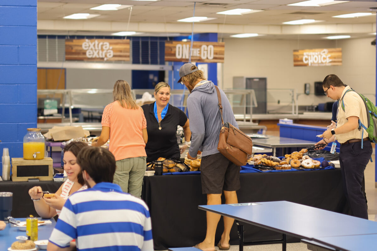 People select pastries from a food service counter in a brightly lit cafeteria.
