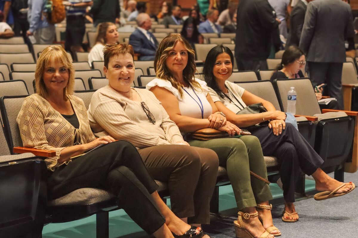 Four women sit in an auditorium, smiling at the camera.