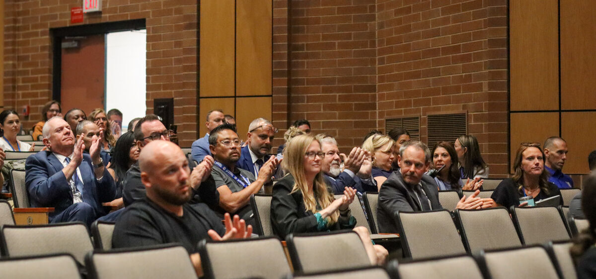 A diverse group of people are seated in an auditorium, clapping their hands.
