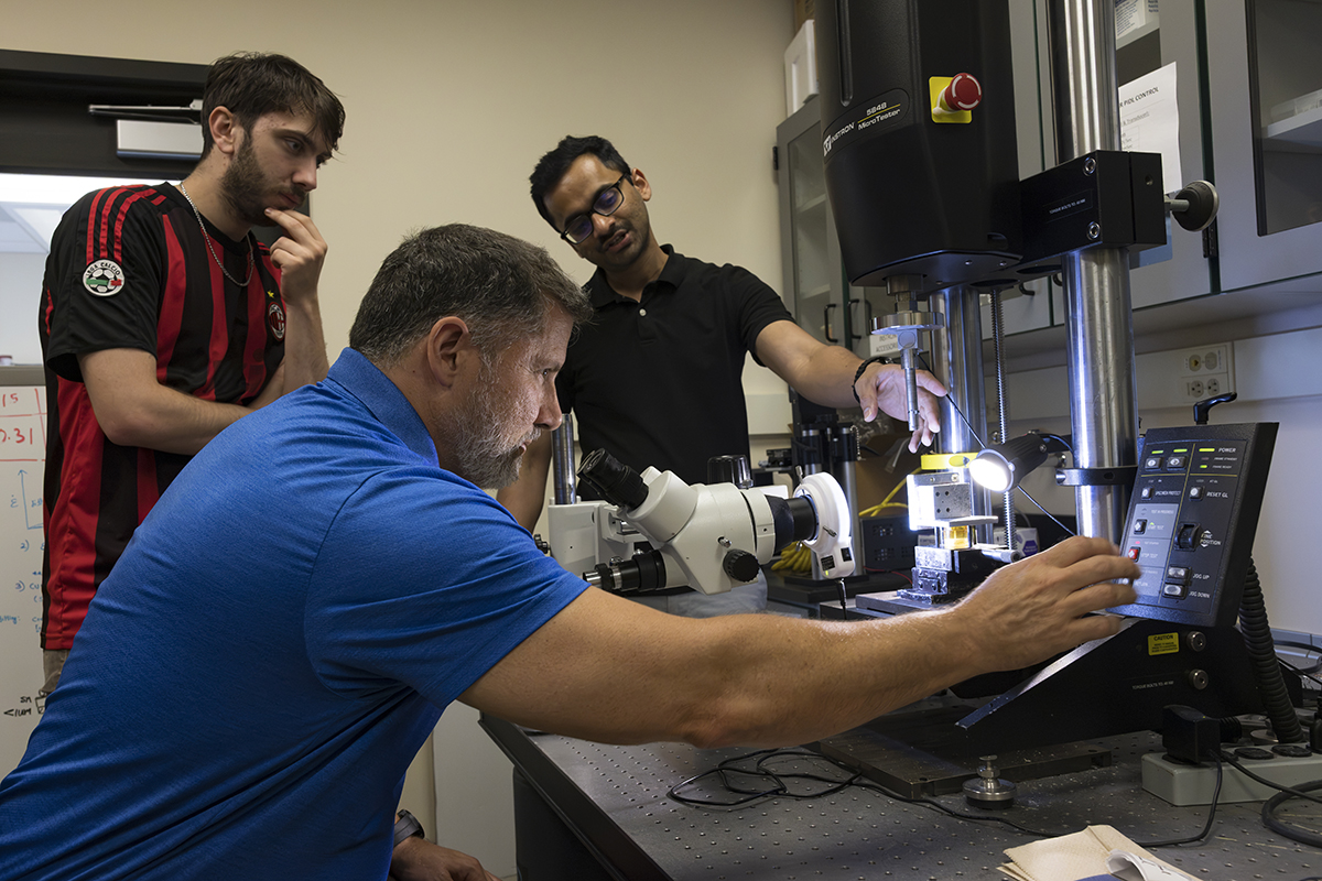 Three individuals collaborate in a laboratory setting, observing a scientific instrument.