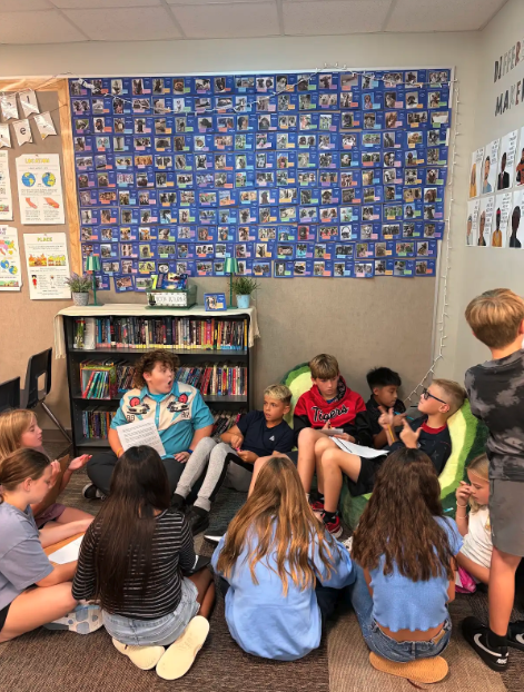 A group of students sit in a circle on a classroom floor, participating in a group activity.