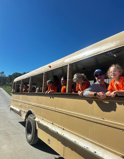 A group of people wearing orange shirts ride in an open-air safari truck on a sunny day.
