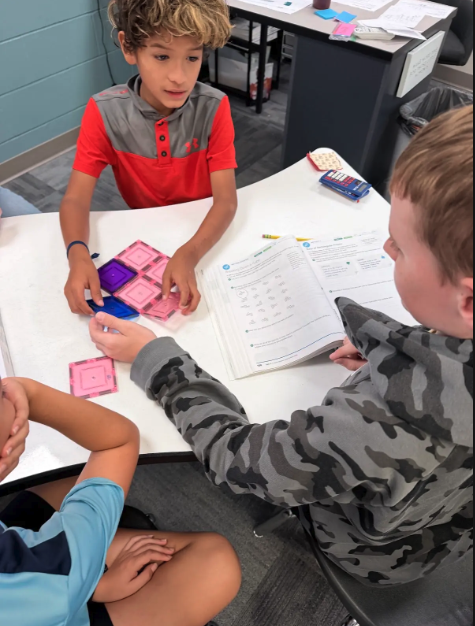 Three students work together at a white table, engaging in a classroom learning activity.