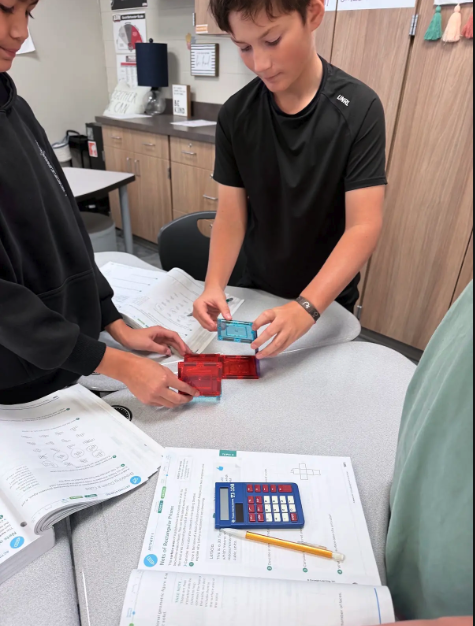 Students gather around a desk in a classroom, working collaboratively with magnetic tiles.